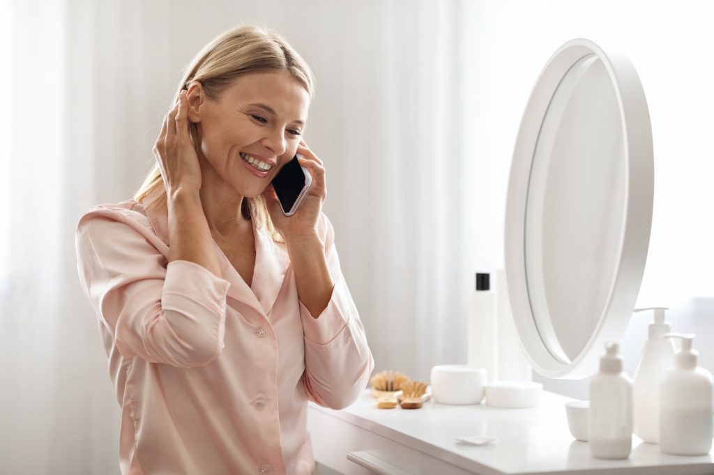 Happy Middle Aged Woman Talking On Cellphone While Sitting At Dressing Table